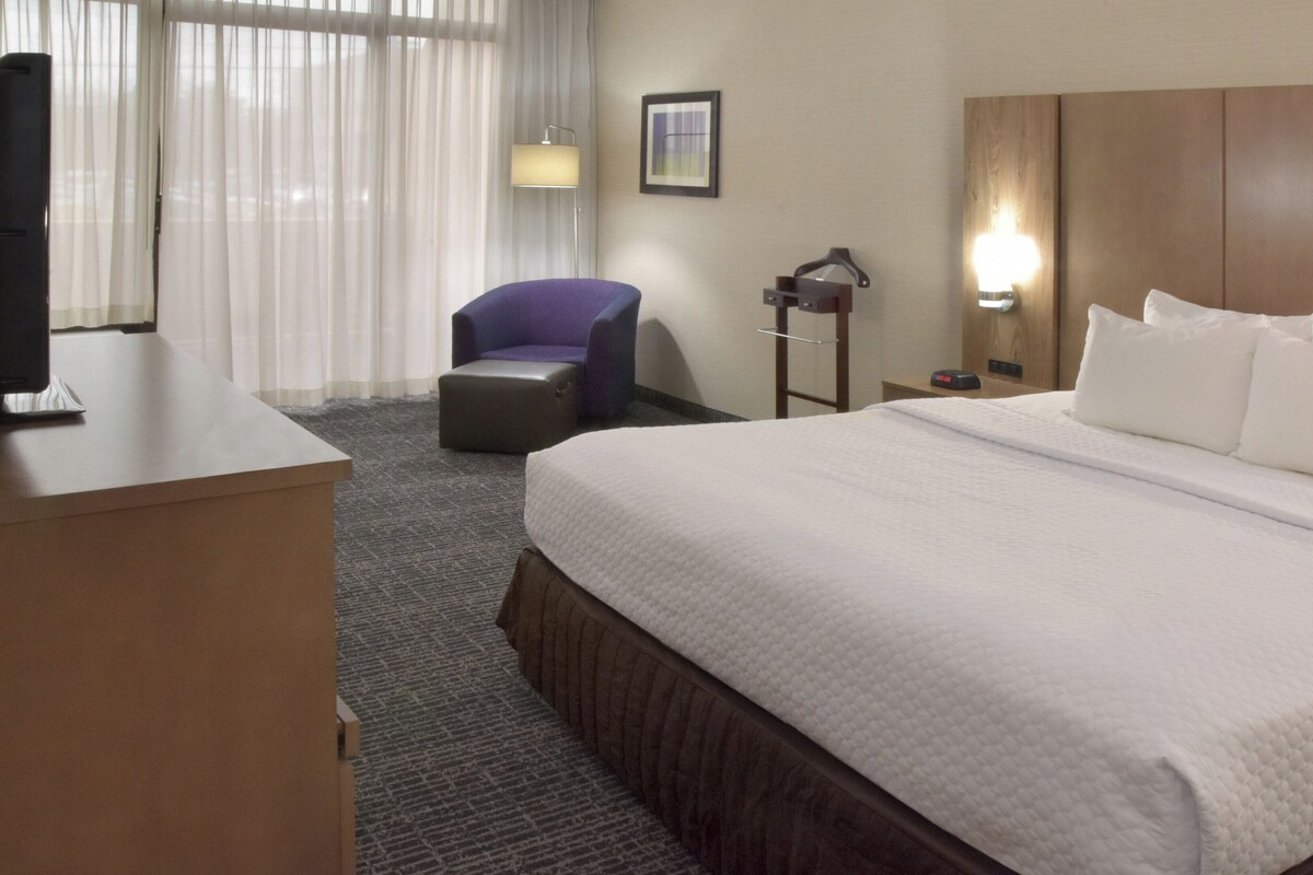 A hotel room with a bed, a desk, a chair, a lamp, and a picture on the wall.