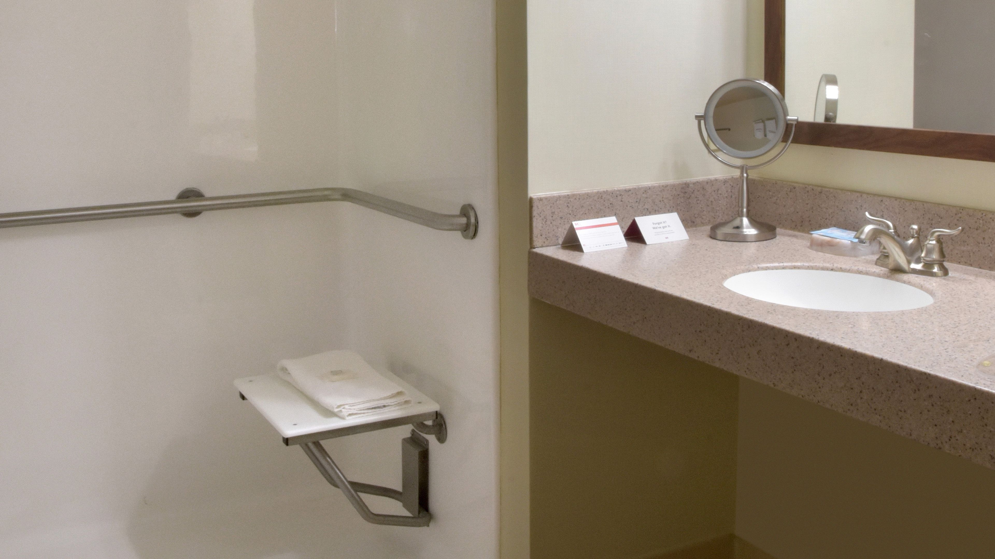 Un baño con barra de apoyo, lavamanos, espejo y toallero.