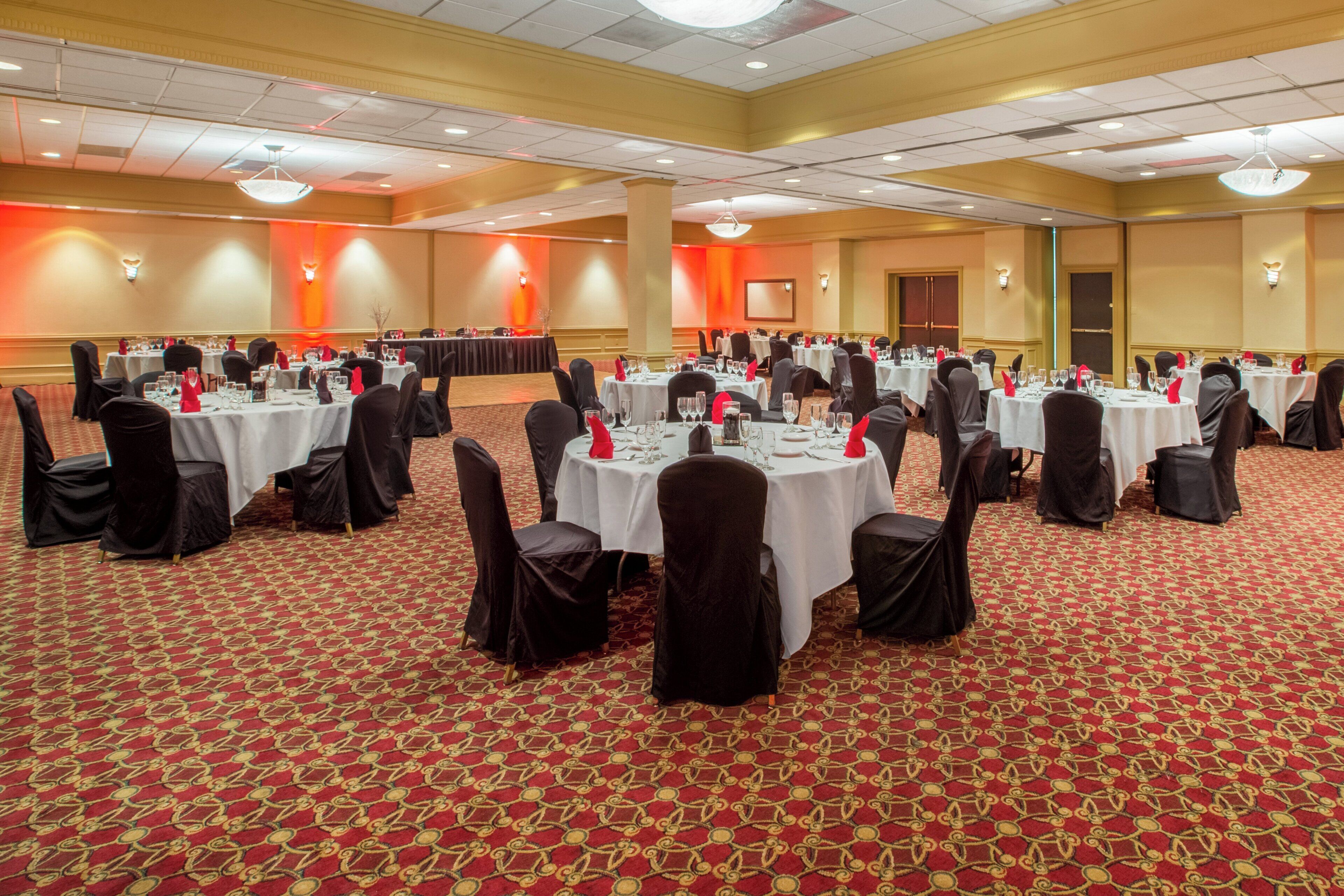 A conference room with multiple round tables, black chairs, and a red patterned carpet.