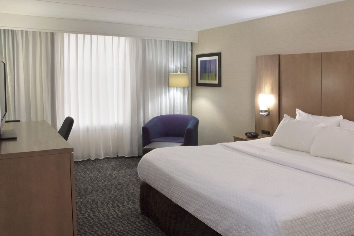 A hotel room with a bed, a desk, a chair, a lamp, and a nightstand.