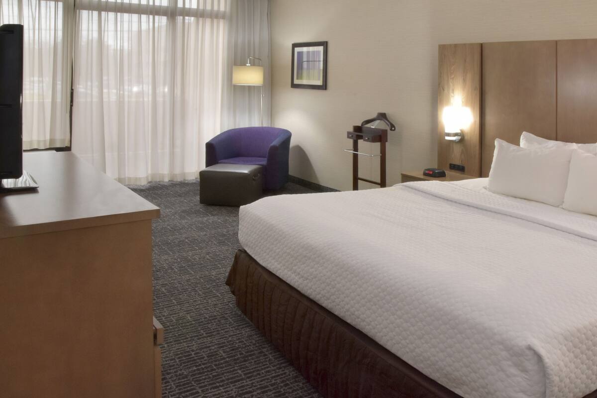 Een hotelkamer met een groot bed, een bureau met een televisie, een paarse stoel en een nachtkastje met een lamp.
