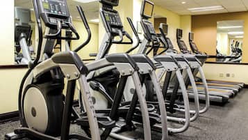 A row of stationary bikes with digital displays, arranged in a gym with mirrored walls.