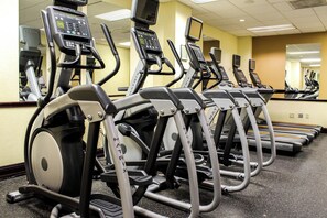 A row of stationary bikes with digital displays, arranged in a gym with mirrored walls.