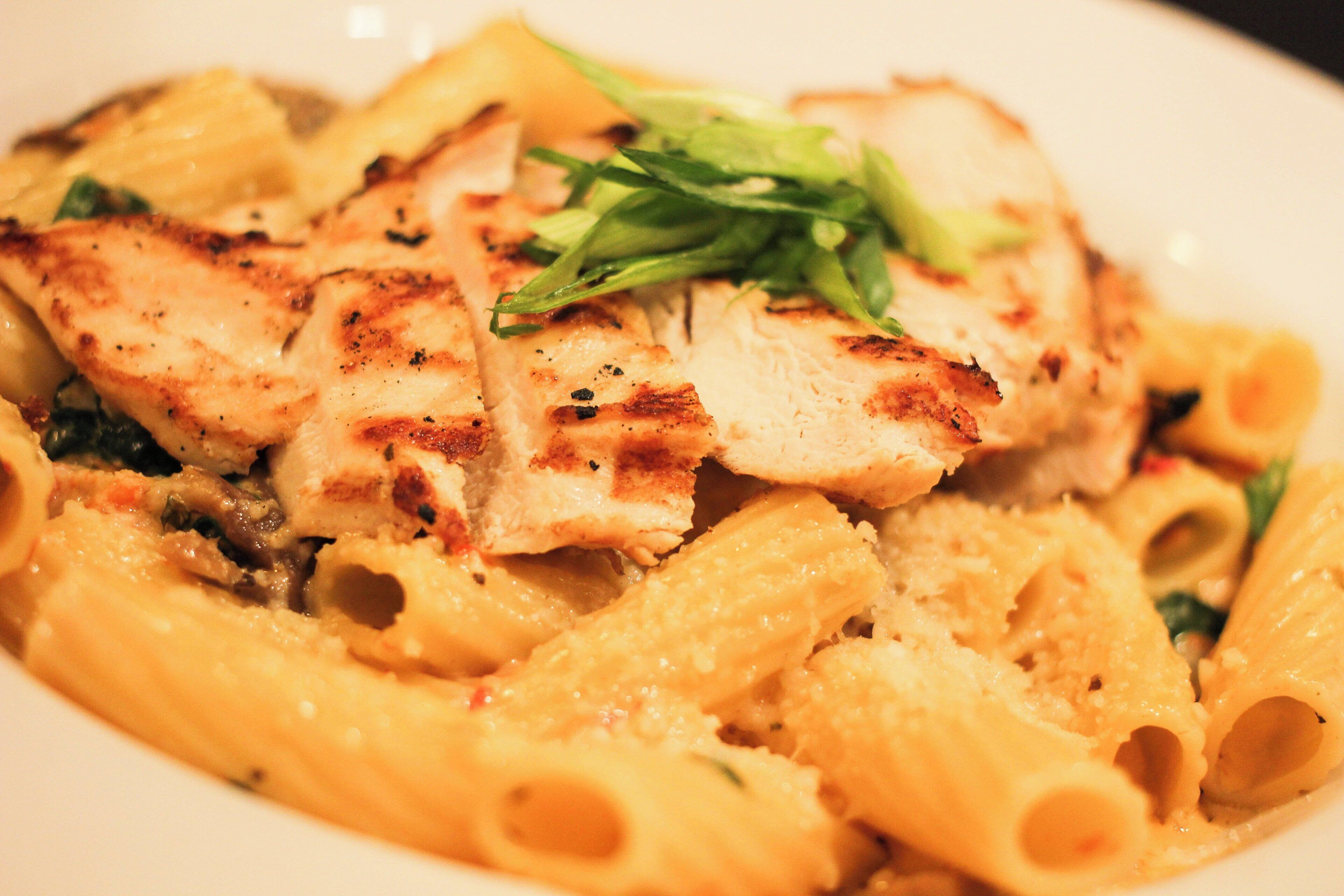 A plate of pasta with grilled chicken and a garnish of green leaves.