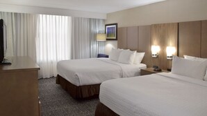 Een hotelkamer met twee bedden, een bureau, een stoel, een televisie en een schilderij aan de muur.