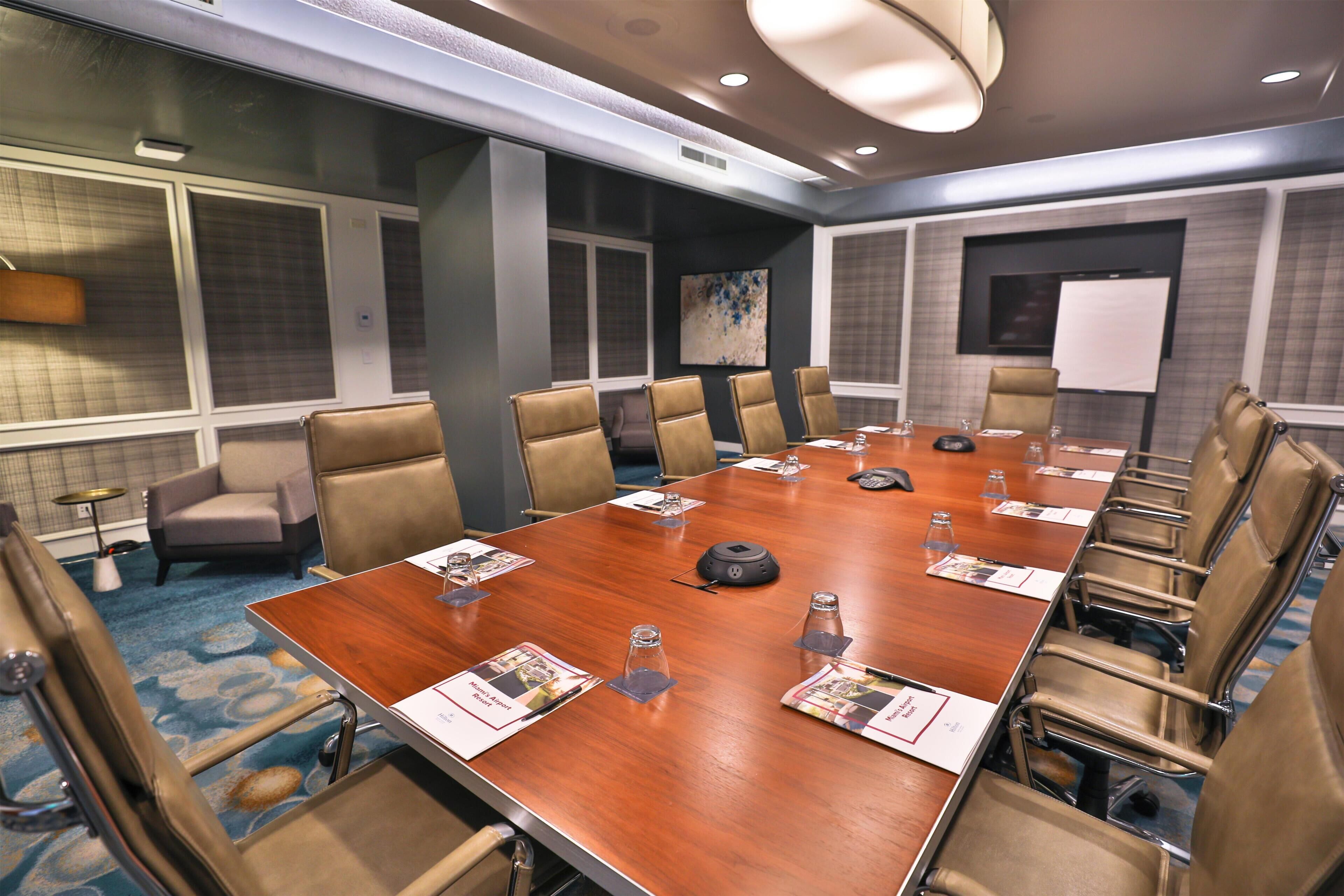 A conference room with a long table, multiple chairs, name cards, and a projector screen.