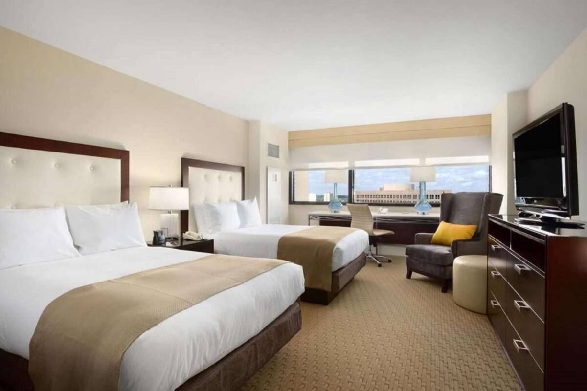 A hotel room with two beds, a desk, a chair, a TV, and a window with a view.
