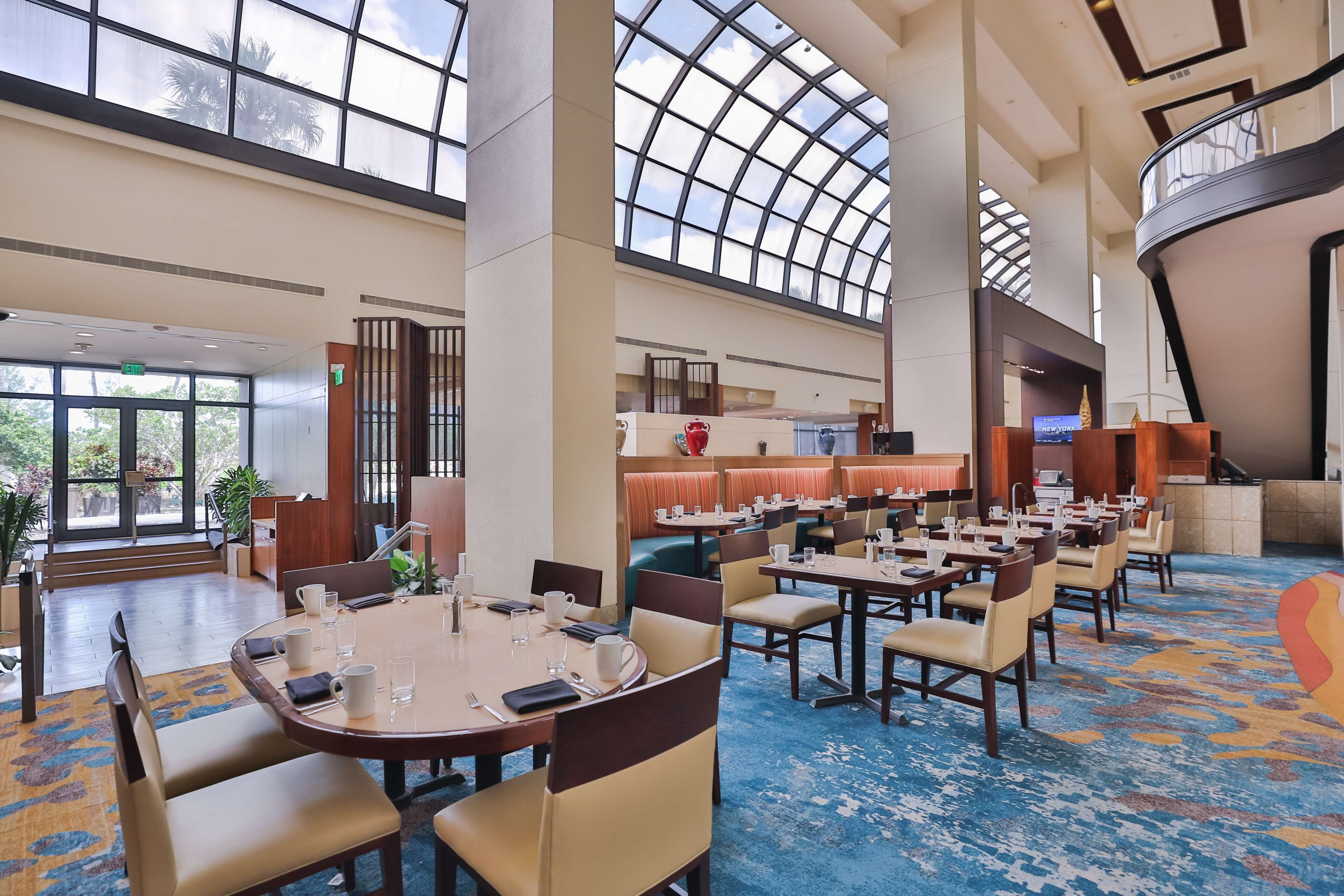 A spacious hotel lobby with high ceilings, a central seating area, and a view of the outdoors.