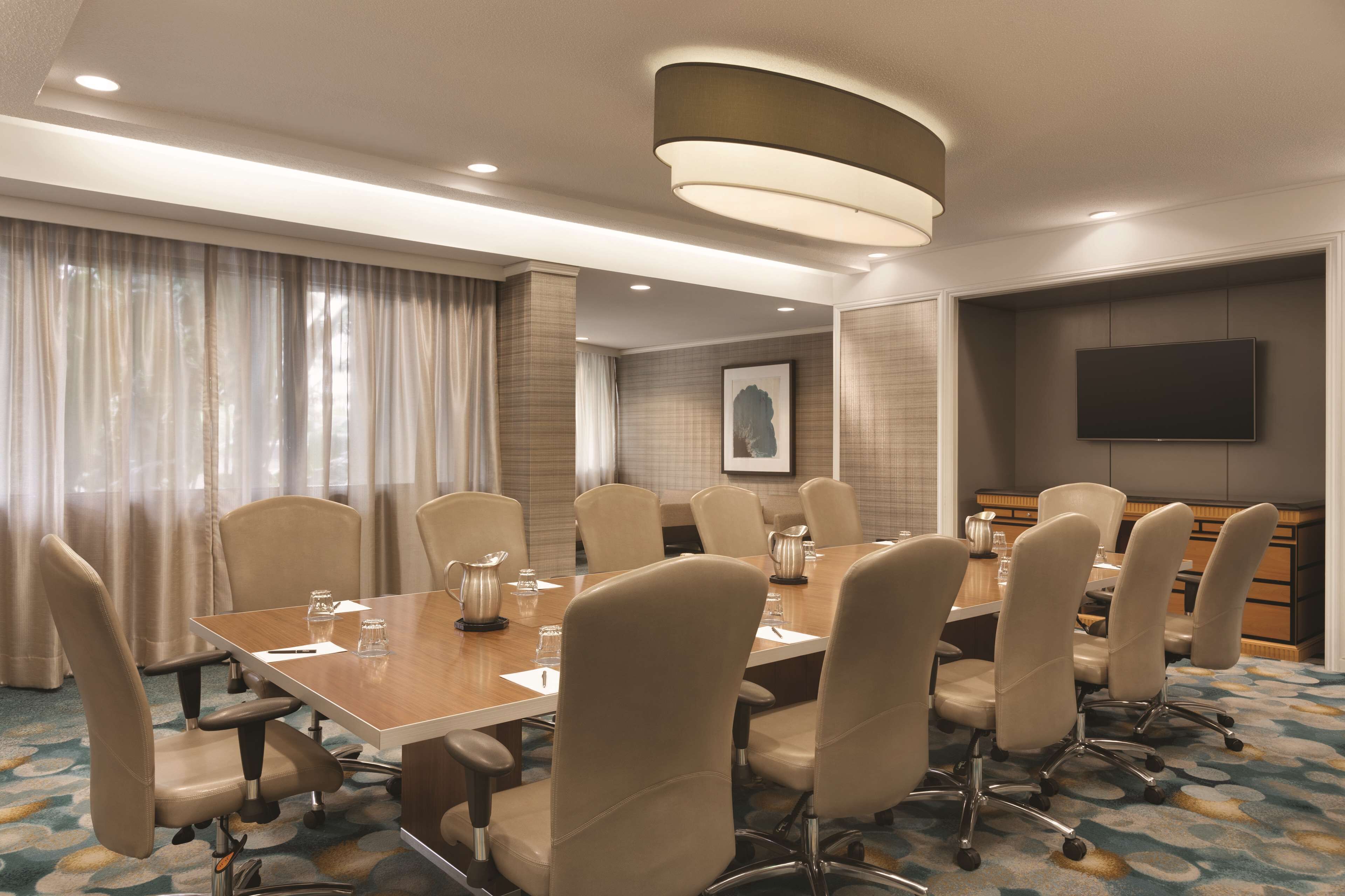 A conference room with a long table, multiple chairs, a television, and a large window with curtains.