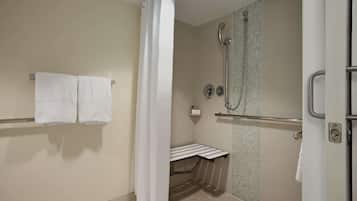 A shower with a glass door, a towel rack with two towels, and a small shelf with a bottle.