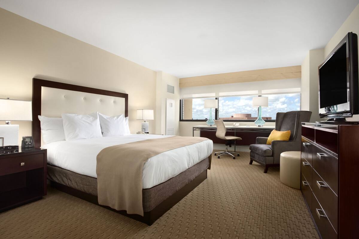 A hotel room with a large bed, a desk, a chair, a television, and a window with a view.