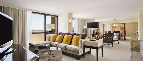A modern hotel room with a sofa, TV, and a dining area.
