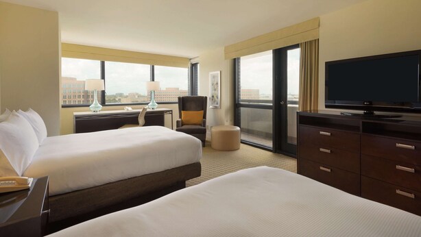 A hotel room with two beds, a TV, a desk with a lamp, a chair, and a large window offering a city view. - Hilton Miami Airport Blue Lagoon (Miami)