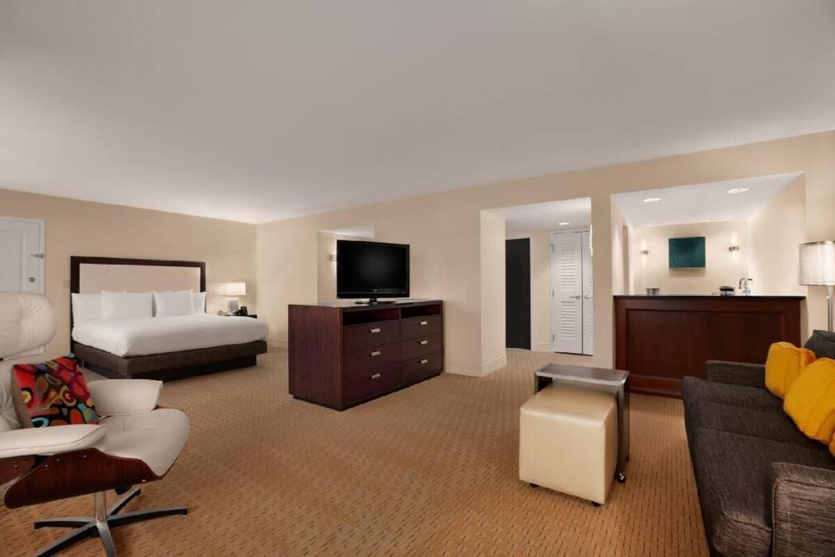 A hotel room with a bed, a TV, a desk, a chair, a sofa, and a small table.