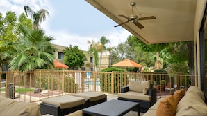 An outdoor patio area with wicker furniture, a ceiling fan, and a view of a swimming pool and palm trees.