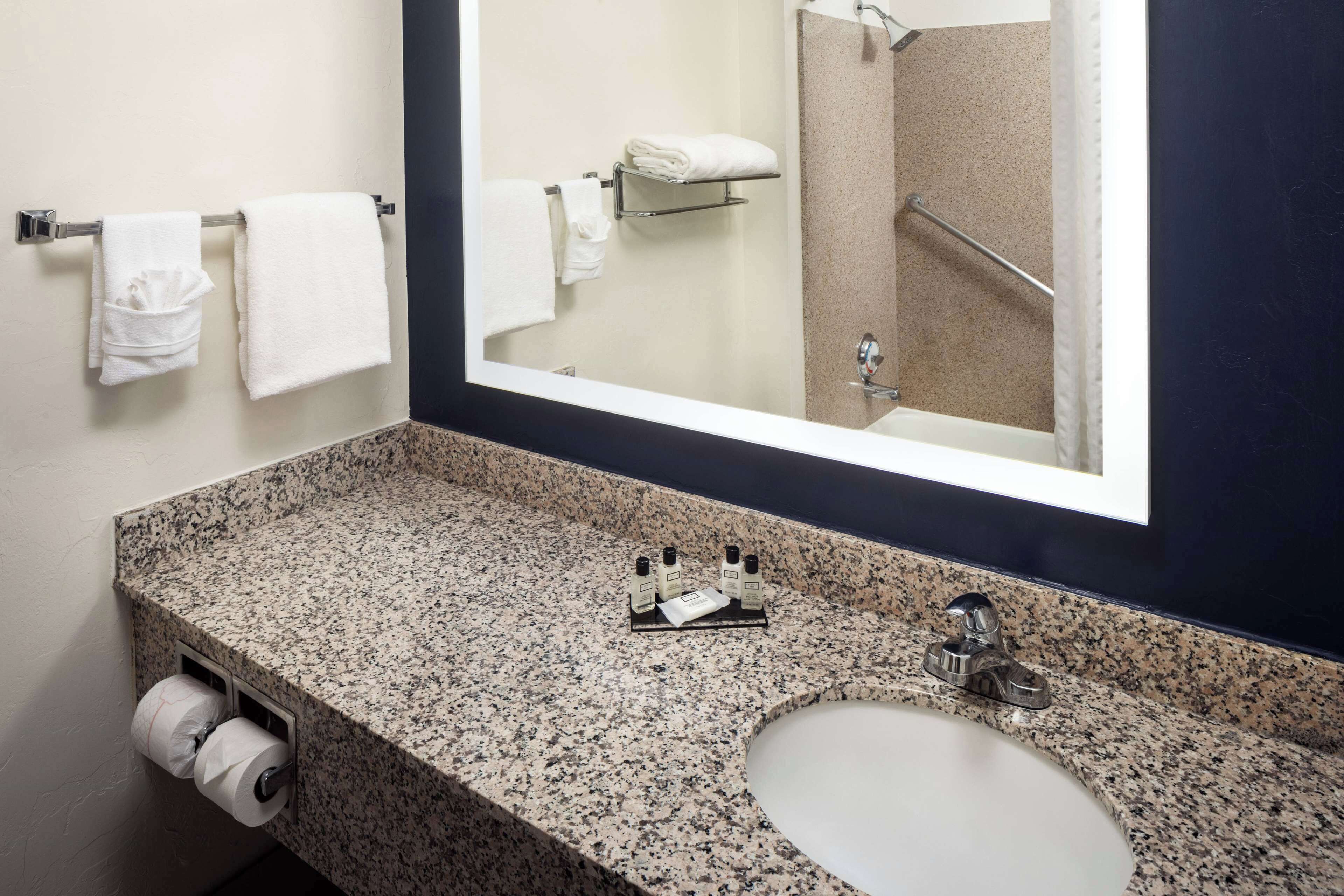 A bathroom with a granite countertop, a sink, a mirror, and a towel rack with folded towels.