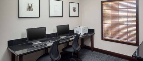 A conference room with three desks, each with a computer and a keyboard. There are three framed pictures on the wall.