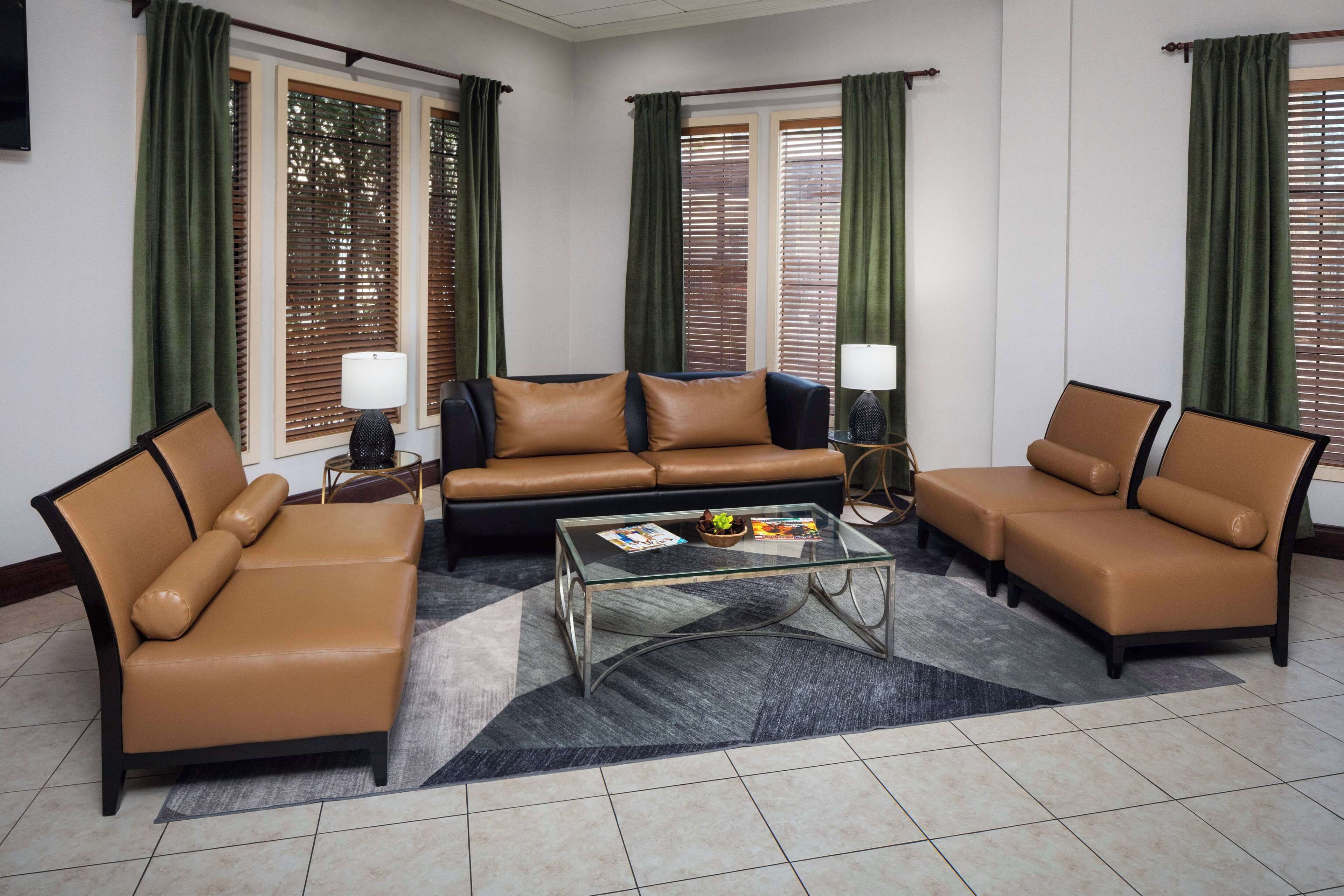 A living room with a brown leather sofa, two armchairs, a glass coffee table, and a side table with a lamp.
