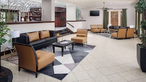 A spacious lobby with a black sofa, brown armchairs, a coffee table, and a large potted plant.