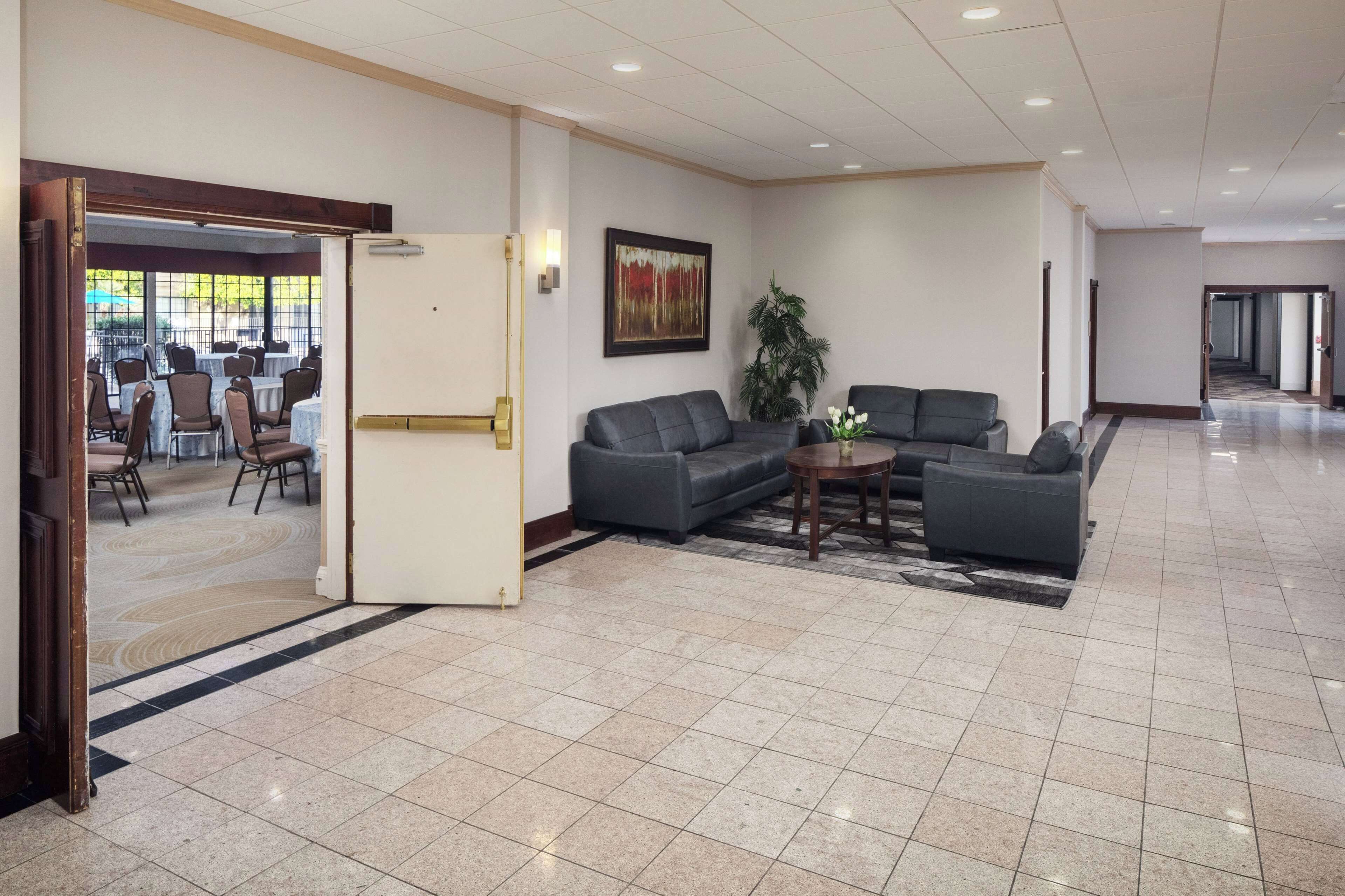 A spacious lobby with a tiled floor, a seating area with sofas and a coffee table, a reception desk, and a framed artwork on the wall.