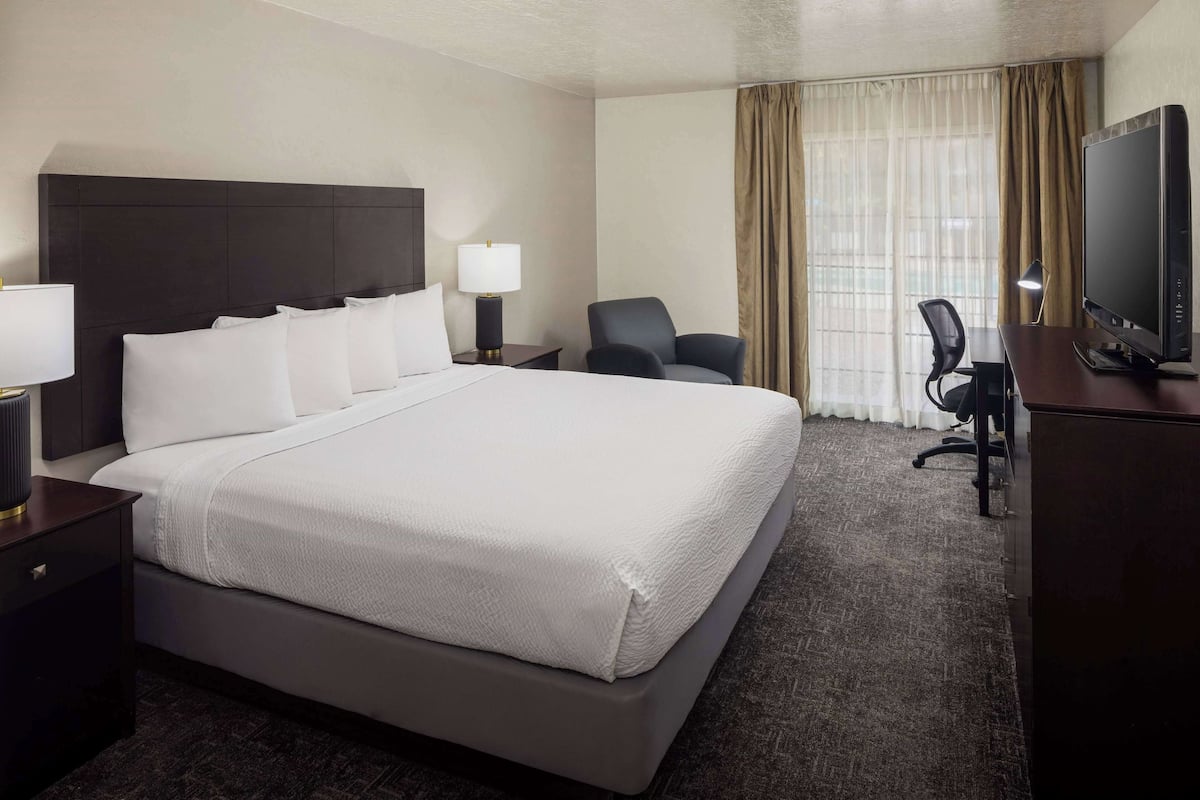 A hotel room with a large bed, a desk with a computer, a chair, and a TV.