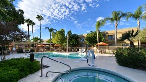 Zona de piscina con varias piscinas, palmeras y mobiliario exterior.
