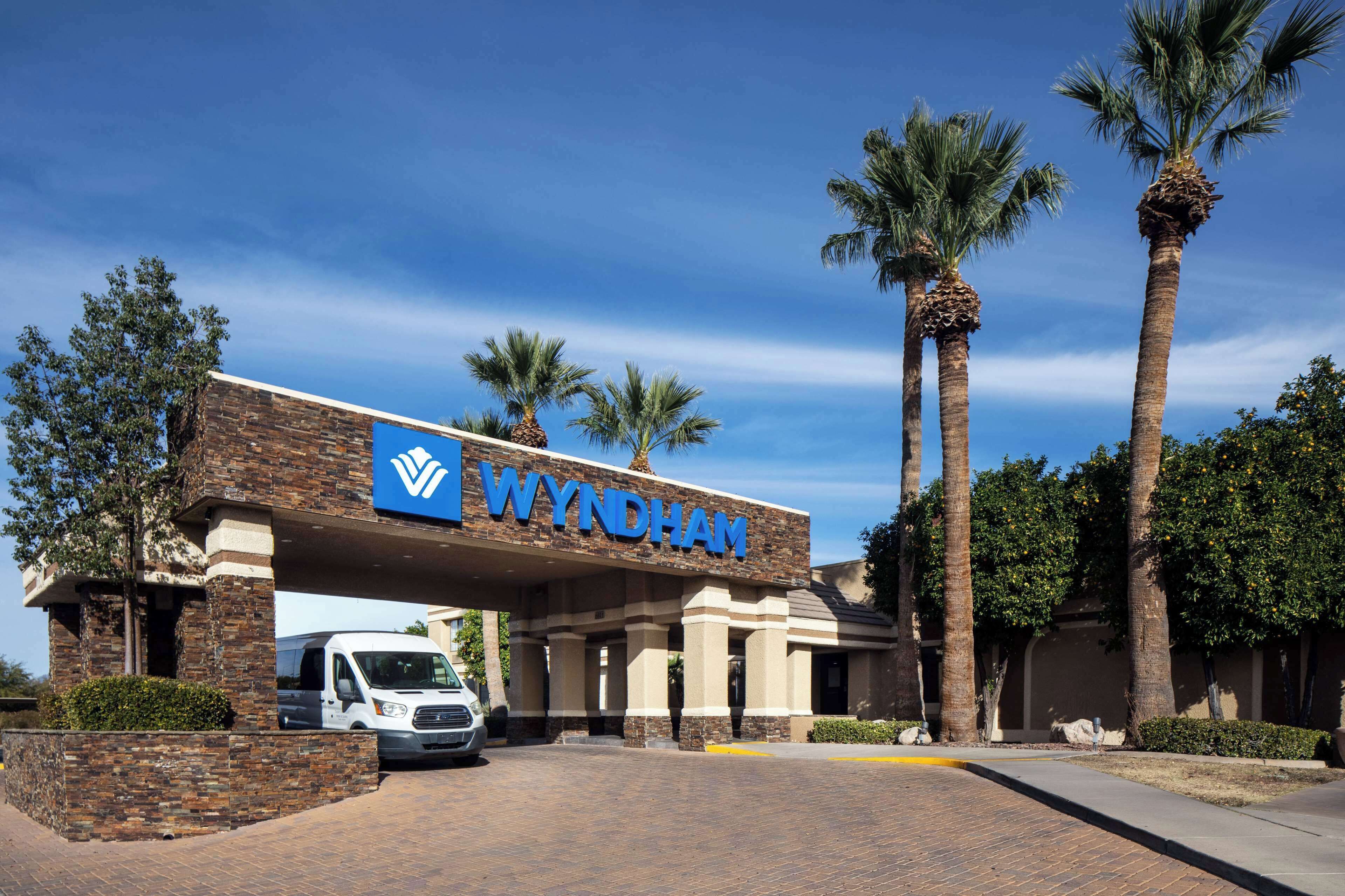 A Wyndham hotel entrance with a brick facade, palm trees, and a clear blue sky.
