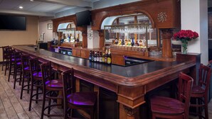 A bar area with wooden bar counters, bar stools, and a variety of bottles.