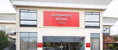 A hotel entrance with a prominent red sign reading 'LEONARDO ROYAL Hotels'.