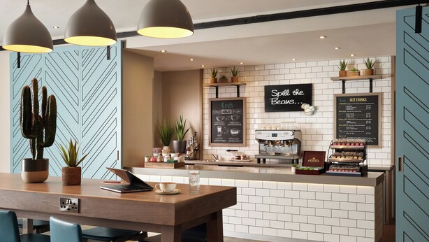 Un café moderne avec un comptoir en bois, des chaises bleues et un menu écrit à la craie.