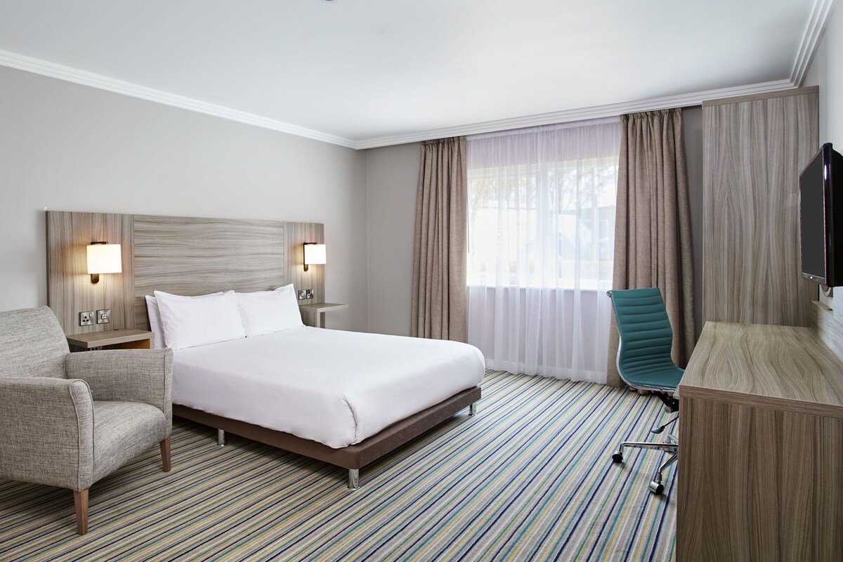 A hotel room with a large bed, a chair, a desk, and a TV.