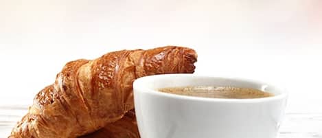 A croissant and a cup of coffee on a white plate with a spoon, set on a wooden surface.