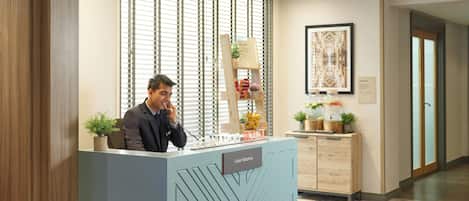 A hotel reception desk with a 'Guest Relations' sign, a welcome sign, and a decorative plant.