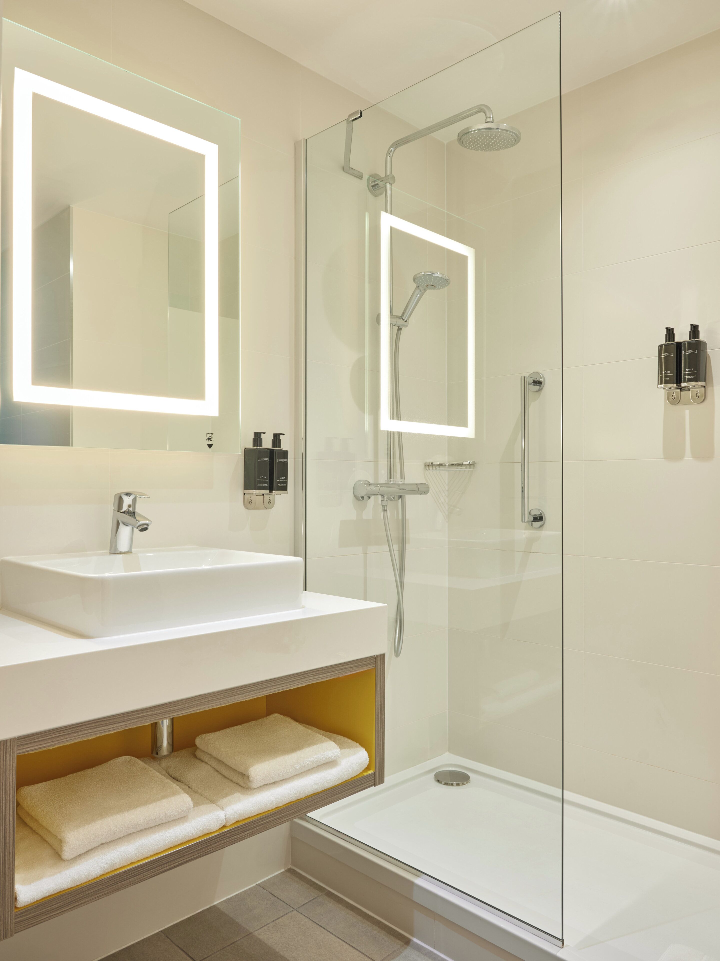 A modern bathroom with a glass-enclosed shower, a vanity with a mirror, and a built-in shelf with towels.