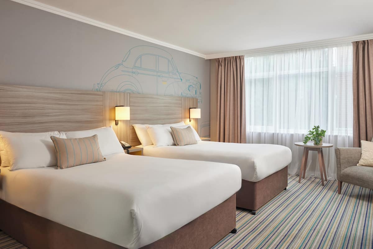 A hotel room with two beds, a small table with a plant, and a window with curtains.