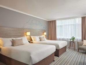 Habitación de hotel con dos camas, una mesita con una planta y una ventana con cortinas.