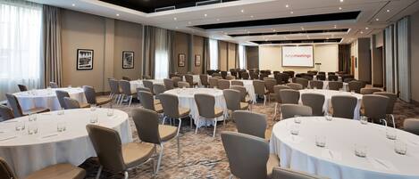 A conference room with multiple round tables, chairs, and a presentation screen.