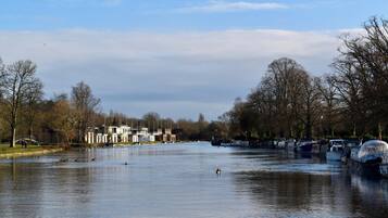 A river with boats docked on the right, a bridge in the background, and leafless trees lining the riverbanks.