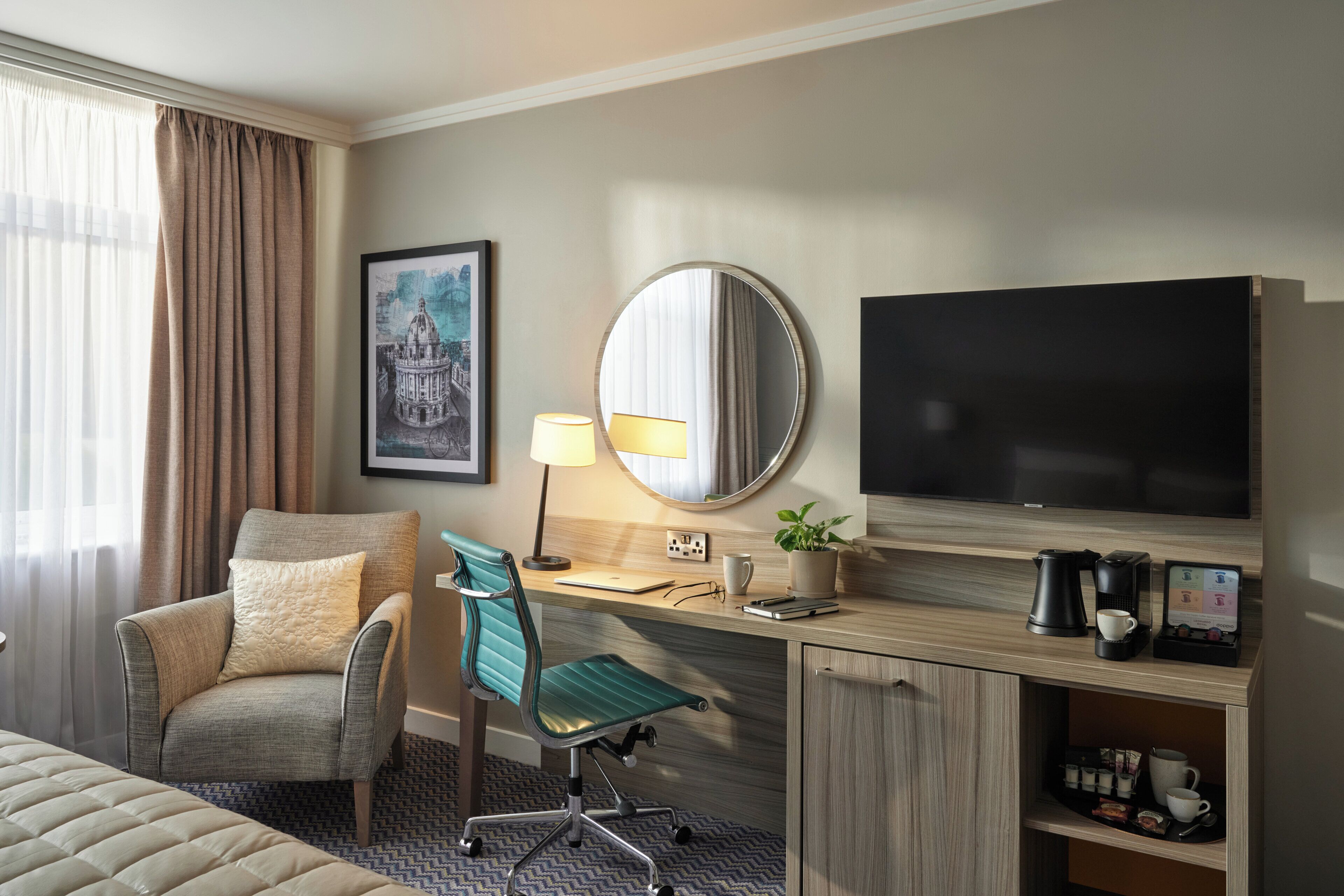 A hotel room with a bed, a desk with a chair, a television, a lamp, and a coffee maker.