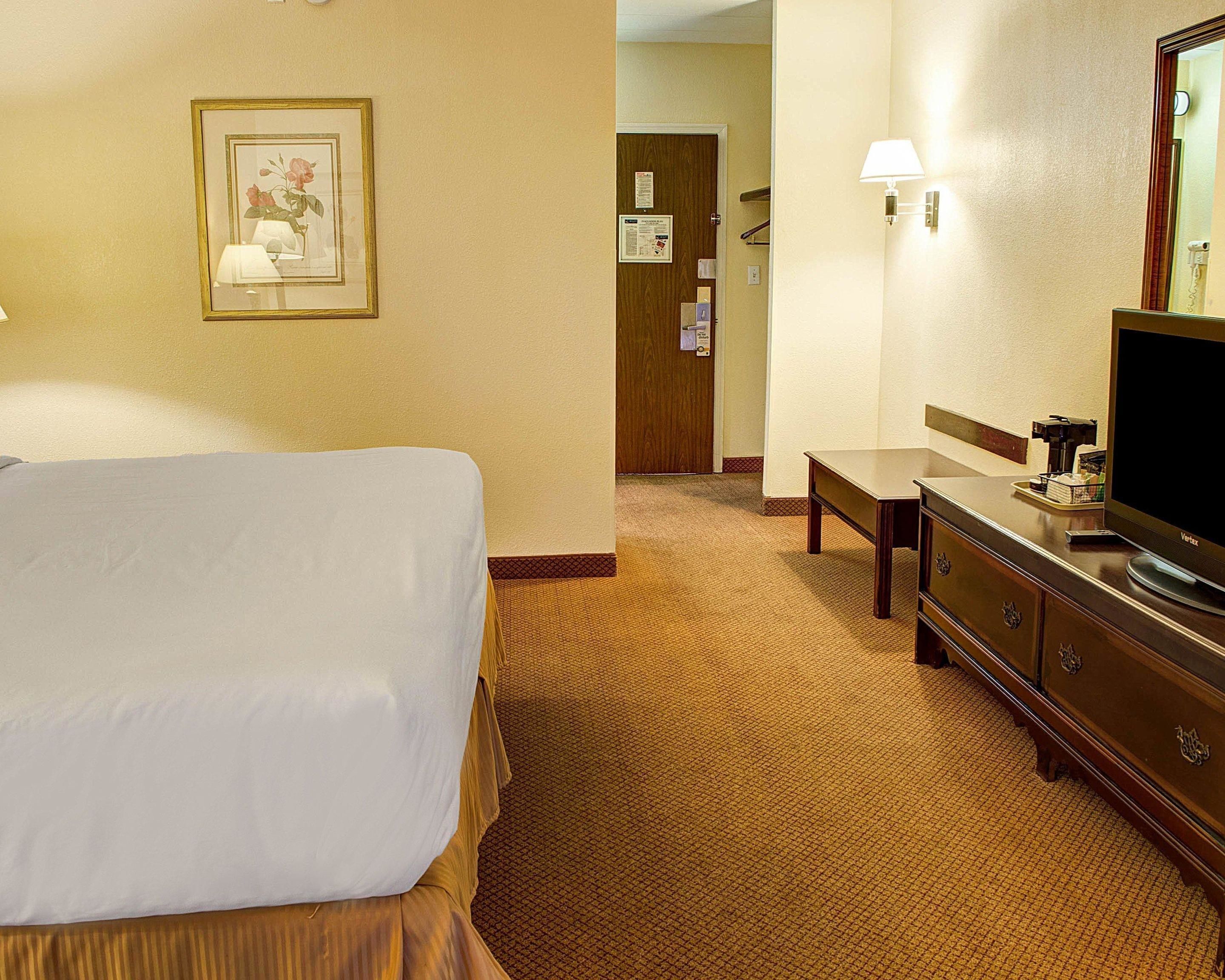 Una habitación de hotel con una cama, un escritorio, una cómoda, una lámpara y un televisor.