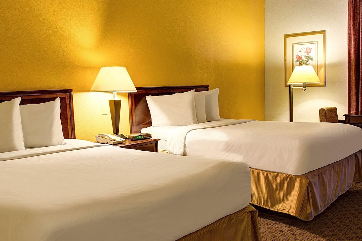 Une chambre d’hôtel avec deux lits, une table de chevet avec une lampe, une horloge et un tableau encadré au mur.
