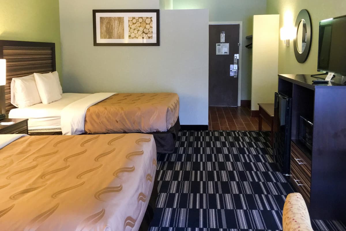 Une chambre d’hôtel avec deux lits, un bureau avec une télévision et une porte donnant sur une salle de bain.