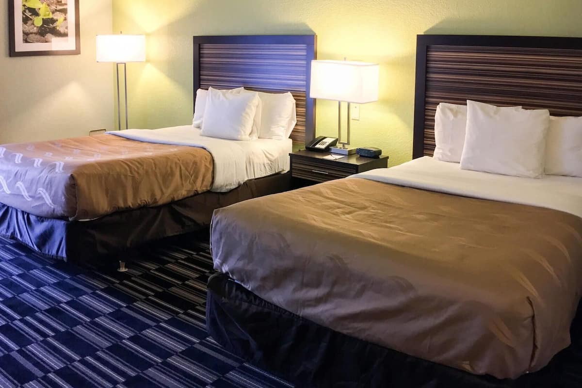 Une chambre d’hôtel avec deux lits, chacun doté d’une tête de lit, de lampes de chevet et d’une table de chevet.