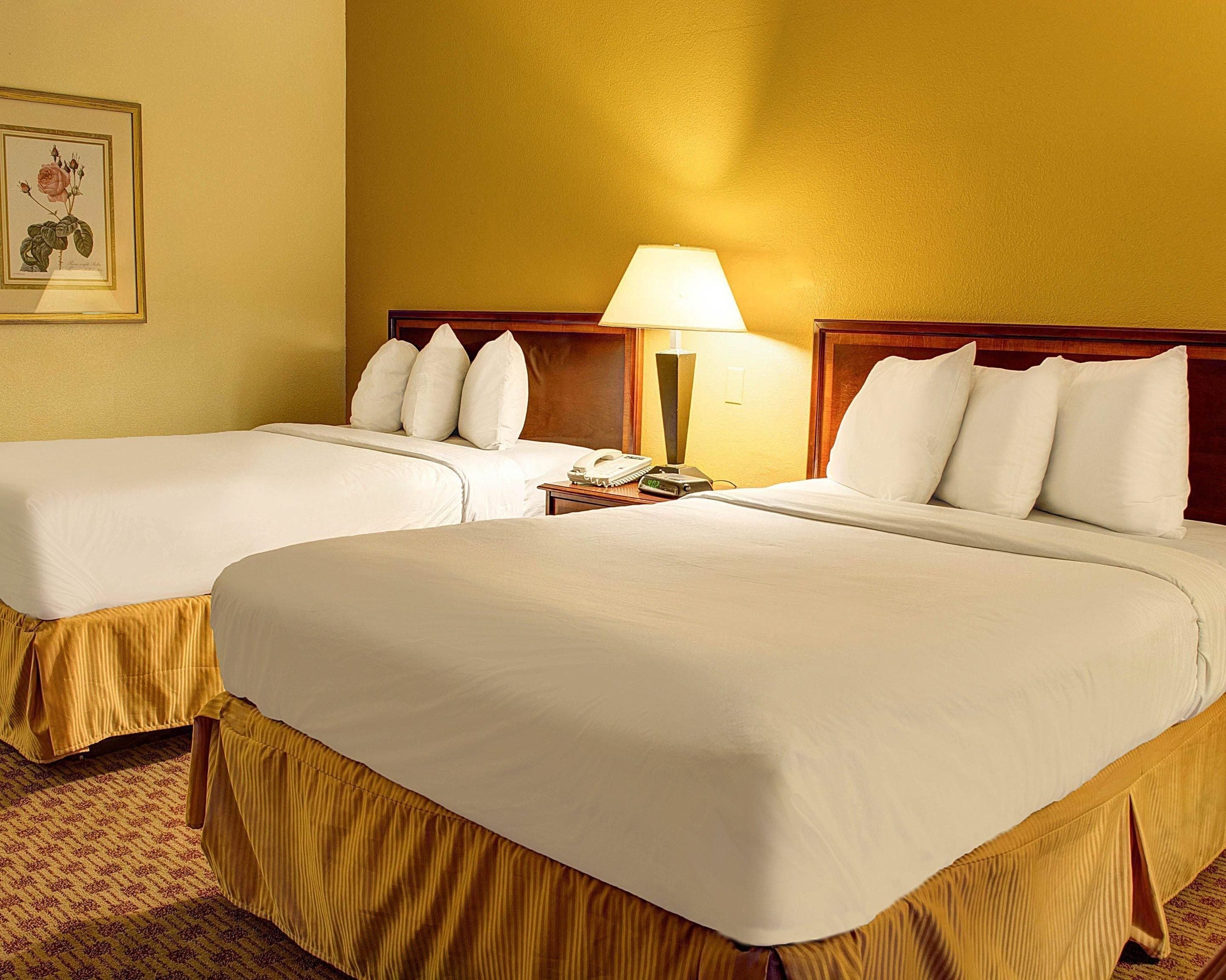 Una habitación de hotel con dos camas, una mesita de noche con lámpara y un cuadro enmarcado en la pared.