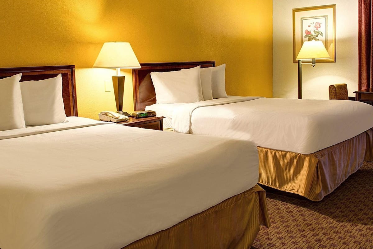Une chambre d’hôtel avec deux lits, une table de chevet avec une lampe, une horloge et un tableau encadré au mur.