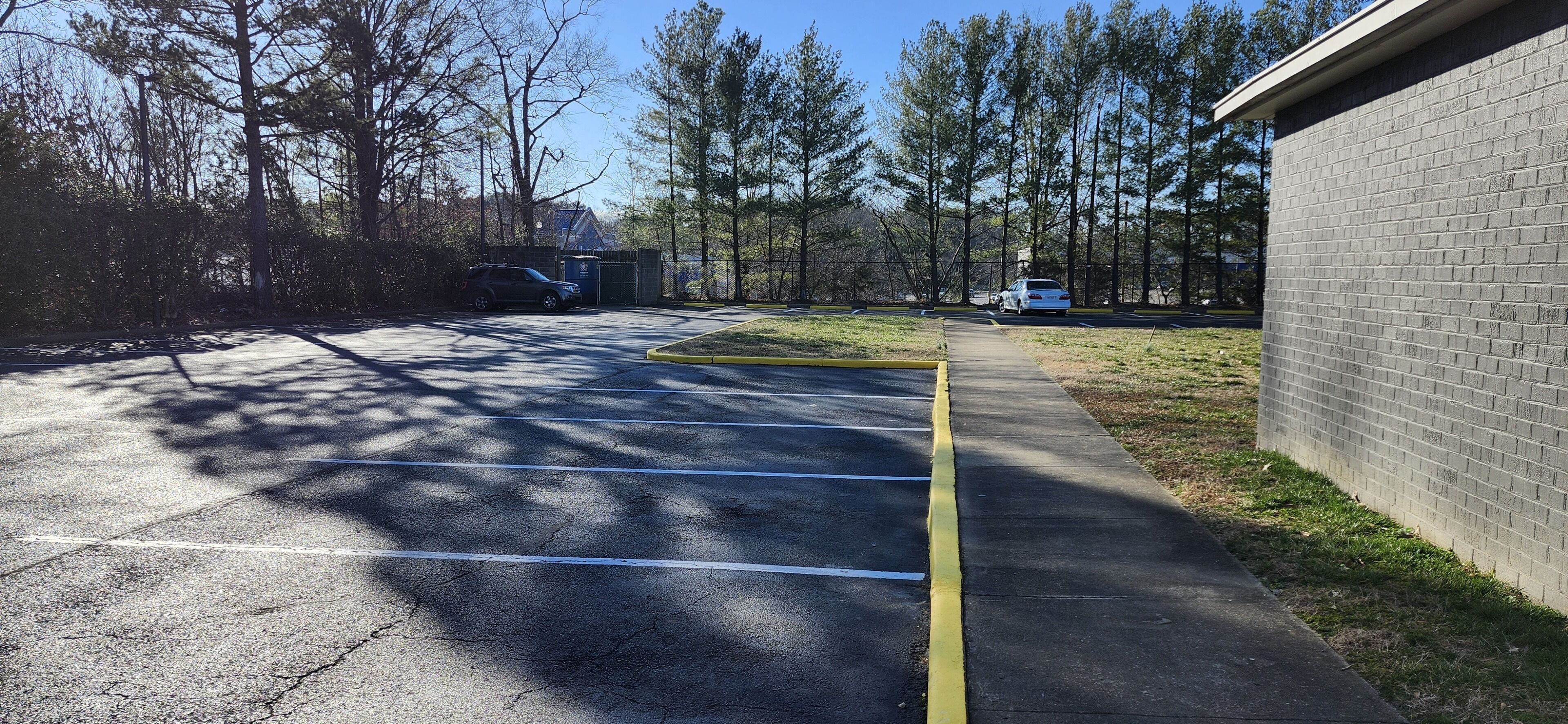 A parking lot with marked spaces, a yellow curb, and a building with a brick facade.