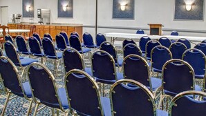 Ett konferensrum med rader av blå stolar, ett långt bord och en talarstol.