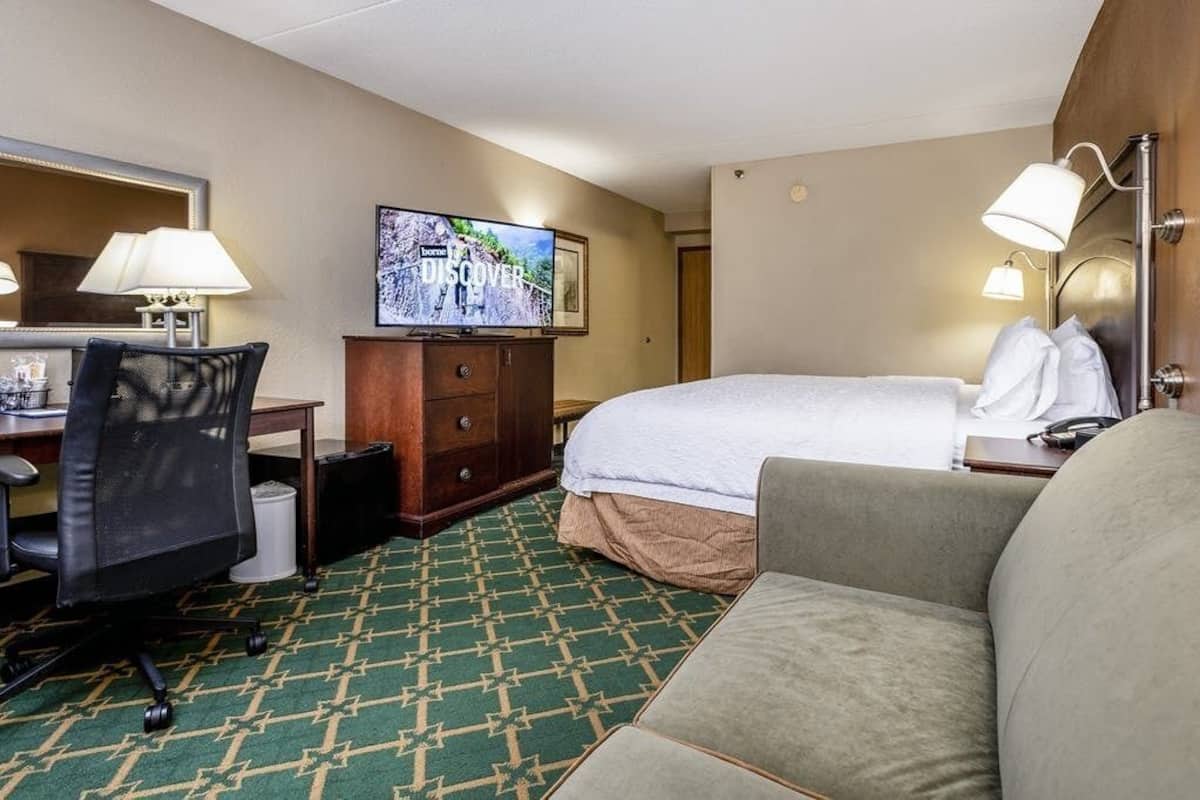 A hotel room with a bed, a desk with a chair, a television, and a sofa.