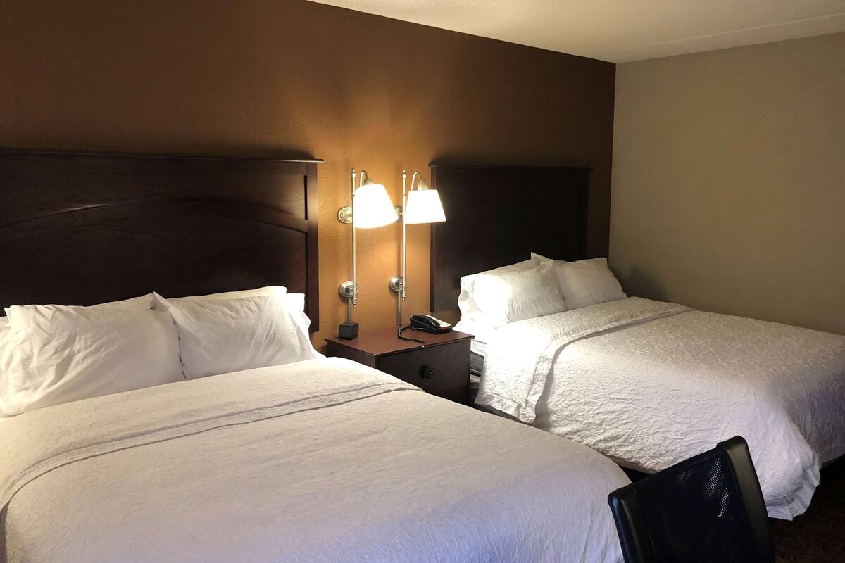 A hotel room with two single beds, a nightstand with a lamp, and a chair.