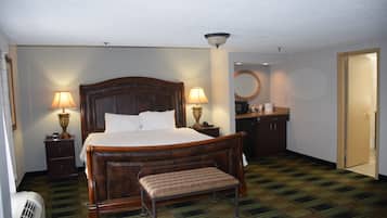 Habitación de hotel con una cama grande, lámparas de noche, un banco, un espejo, un escritorio y una puerta.